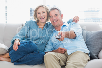 Cheerful couple cuddling and sitting on the couch watching tv