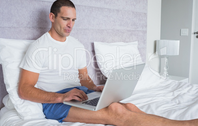 Concentrating man using laptop on bed