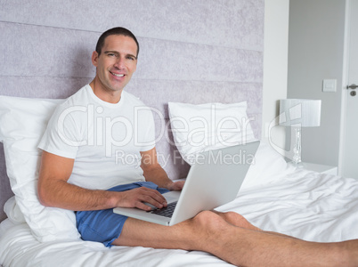 Happy man using laptop on bed