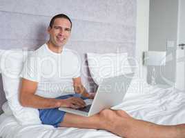 Happy man using laptop on bed