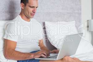 Serious man using laptop on bed