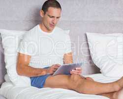 Cheerful man using tablet pc on bed