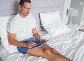 Smiling man using his tablet pc on bed