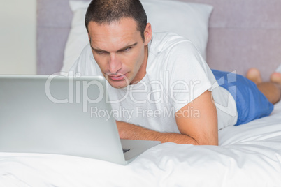 Concentrated man lying on bed using his laptop