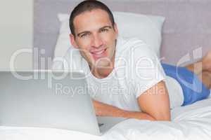 Happy man lying on bed using his laptop