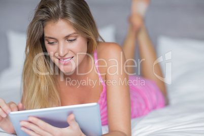 Happy blonde lying on her bed using her tablet pc