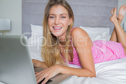 Cheerful blonde lying on her bed using her laptop