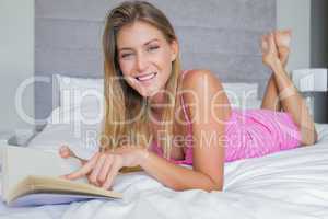 Smiling blonde lying on her bed reading a book