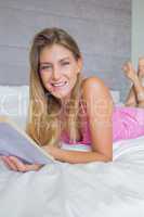 Happy blonde lying on her bed reading a book