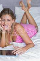 Beautiful blonde lying on her bed using tablet pc smiling at cam