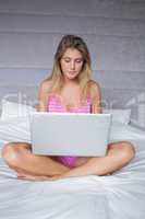 Smiling blonde woman sitting on her bed using laptop