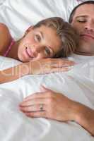 Happy woman lying on husbands chest in bed