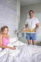Smiling woman being brought breakfast in bed by husband