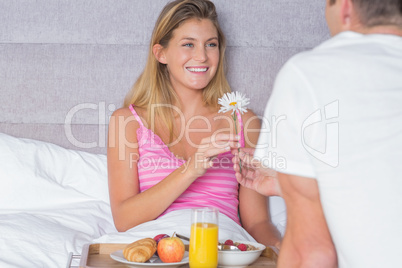 Happy woman taking a daisy from partner at breakfast in bed