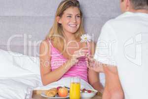 Happy woman taking a daisy from partner at breakfast in bed