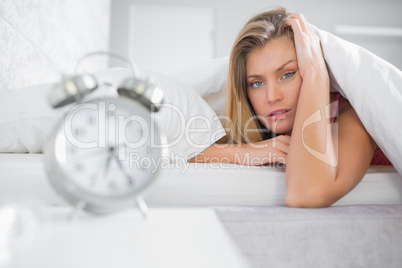 Exhausted blonde looking at camera with alarm clock in foregroun