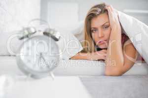 Exhausted blonde looking at camera with alarm clock in foregroun