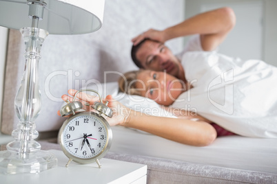 Tired couple looking at alarm clock in the morning with woman tu