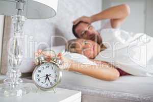 Tired couple looking at alarm clock in the morning with woman tu