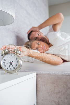 Annoyed couple looking at alarm clock in the morning with woman
