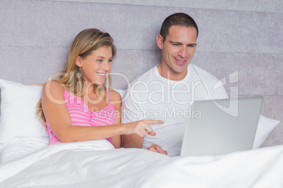 Happy young couple using their laptop together in bed