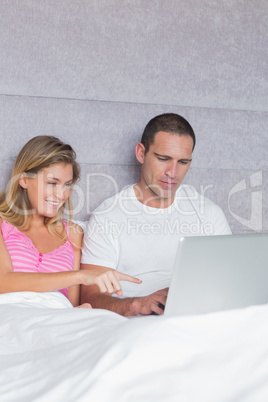 Smiling young couple using their laptop together in bed
