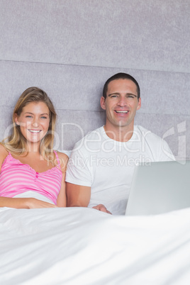 Cheerful young couple using their laptop together in bed