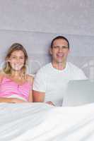 Cheerful young couple using their laptop together in bed