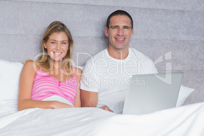 Attractive young couple using their laptop together in bed