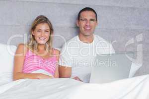 Attractive young couple using their laptop together in bed