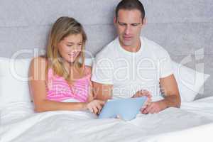 Attractive young couple using their tablet pc together in bed