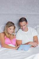 Cute young couple using their tablet pc together in bed