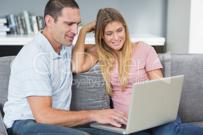 Happy couple sitting using laptop on the couch together