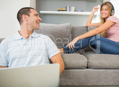 Man sitting on floor with laptop with woman listening to music o