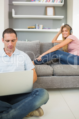 Man sitting on floor using laptop with woman listening to music