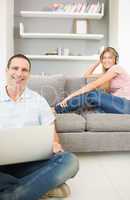 Man sitting on floor using laptop with woman listening to music