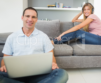 Man sitting on floor using laptop with woman listening to music