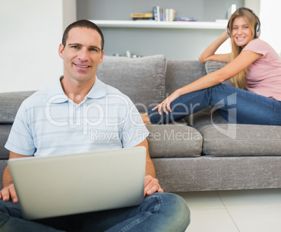 Man sitting on floor with laptop with woman listening to music o