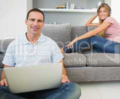 Man sitting on floor with laptop with woman listening to music o