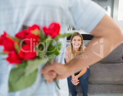 Man hiding bouquet of roses from girlfriend on the couch