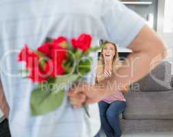 Man hiding bouquet of roses from smiling girlfriend on the couch