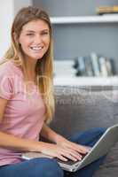 Attractive blonde sitting on her sofa using laptop looking at ca
