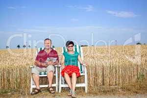 man and woman sitting in the garden chair in front of the field