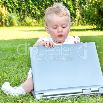 Baby sitting with laptop in a meadow