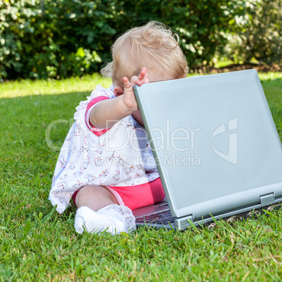 Baby sitting with laptop in a meadow