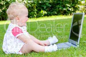 Baby sitting with laptop in a meadow