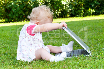 Baby sitting with laptop in a meadow