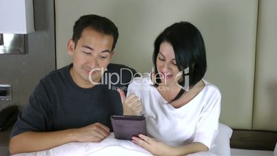 happy couple sitting on bed and looking at the tablet pc having a conference