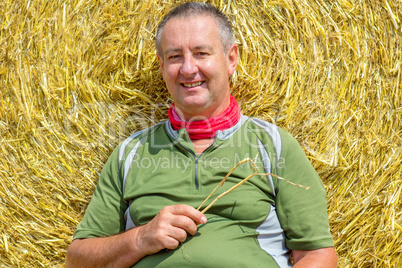 Organic farmer sitting in front of bales of straw