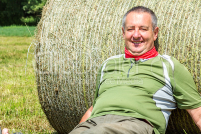 Organic farmer is resting against the hay bales